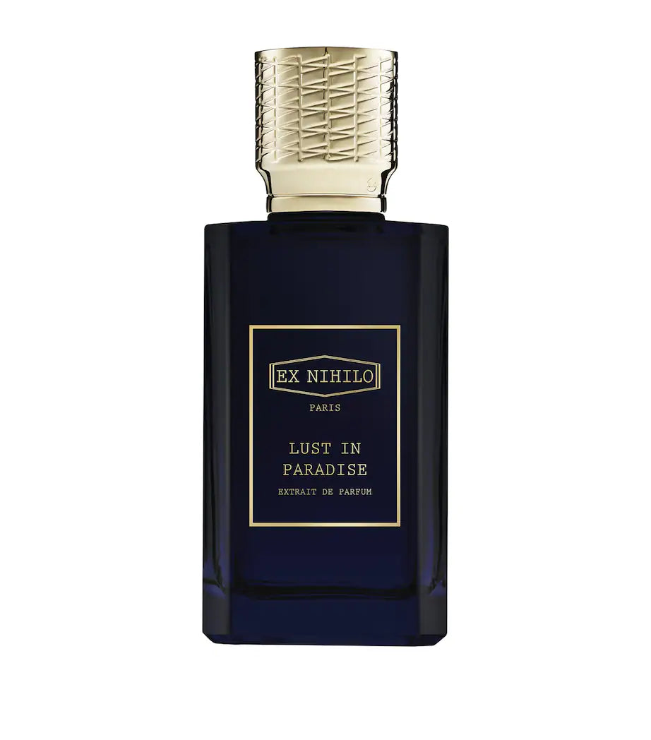 A dark navy blue glass perfume bottle with a textured gold cap and a gold-bordered label reading 'EX NIHILO PARIS LUST IN PARADISE EXTRAIT DE PARFUM'.