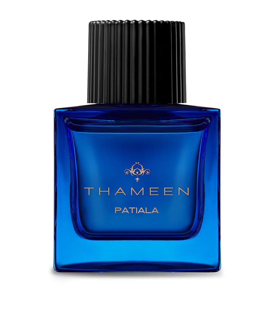 a blue perfume bottle with thameen patiala written in gold text. a black perfume cap on a white background